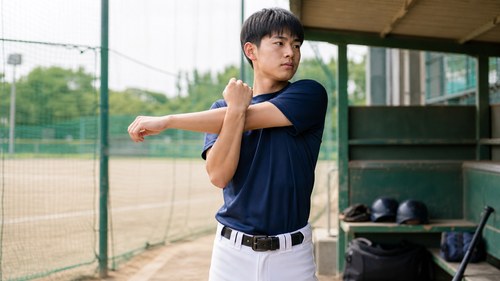 全身の柔軟性を保つため肩腕を伸ばす野球選手