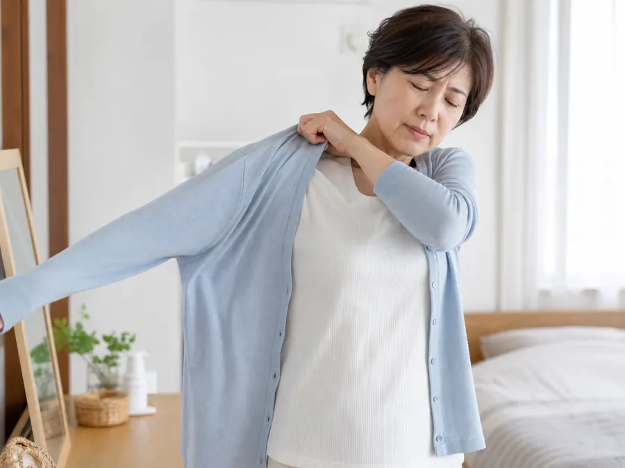 肩をかばいながら上着を着る女性