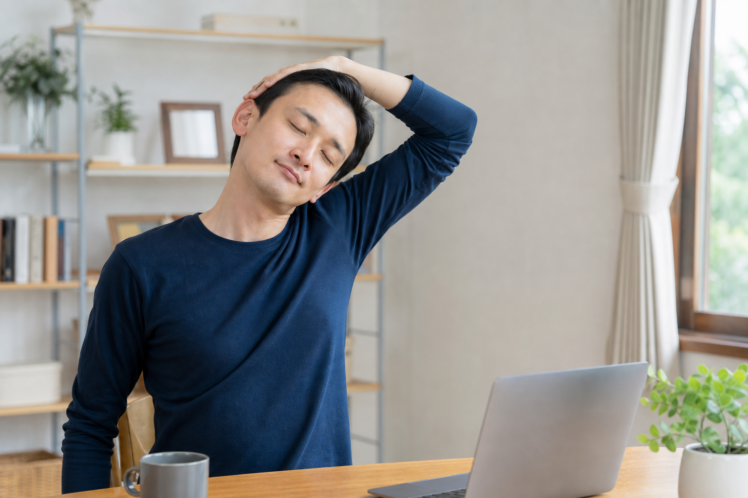 デスク横で首と肩をやさしく伸ばす日本人男性のイメージ