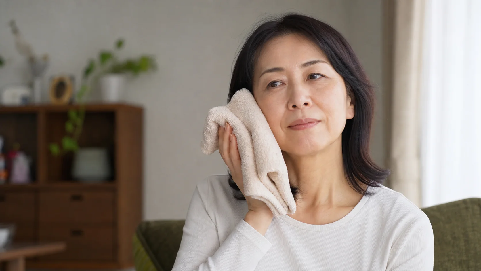 温かいタオルで片側の頬をやさしく温める女性