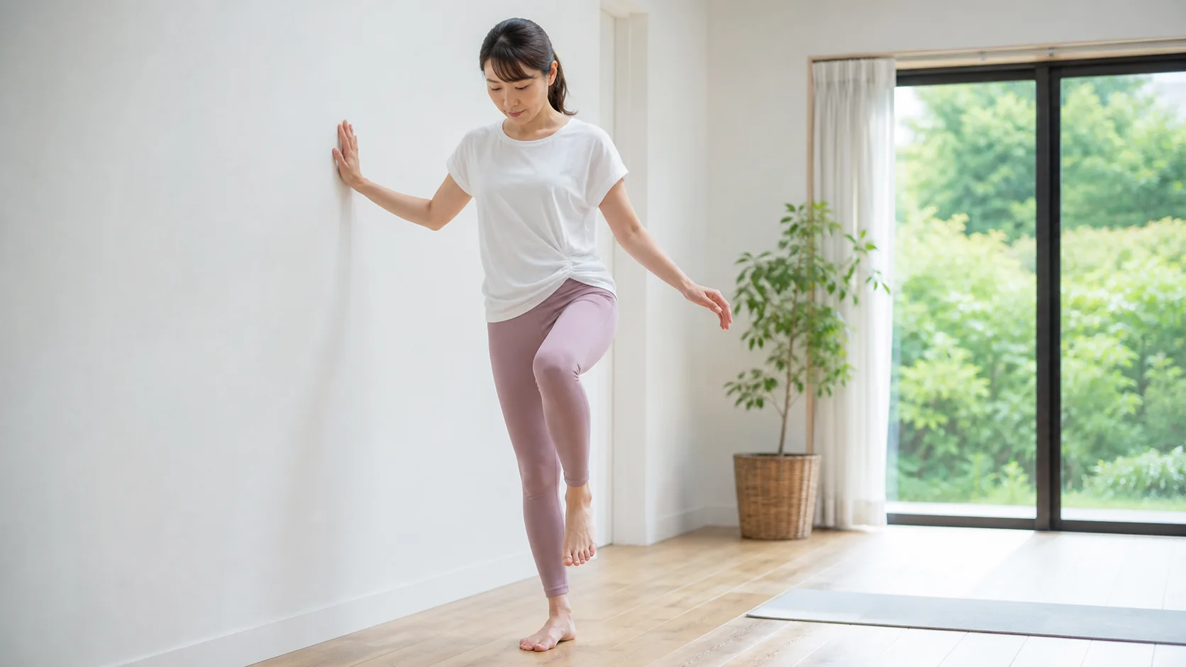 壁に手を添えて片足立ちをする女性