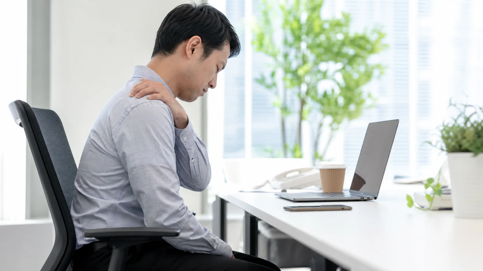 デスクで肩まわりの不調を感じる男性