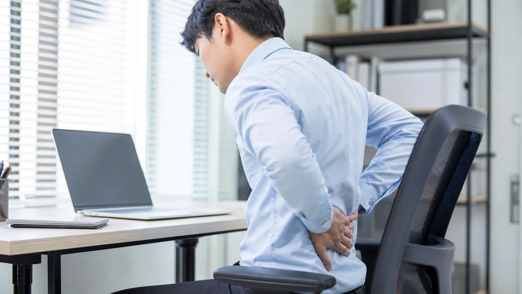 デスクワーク中に背中の痛みを感じる男性