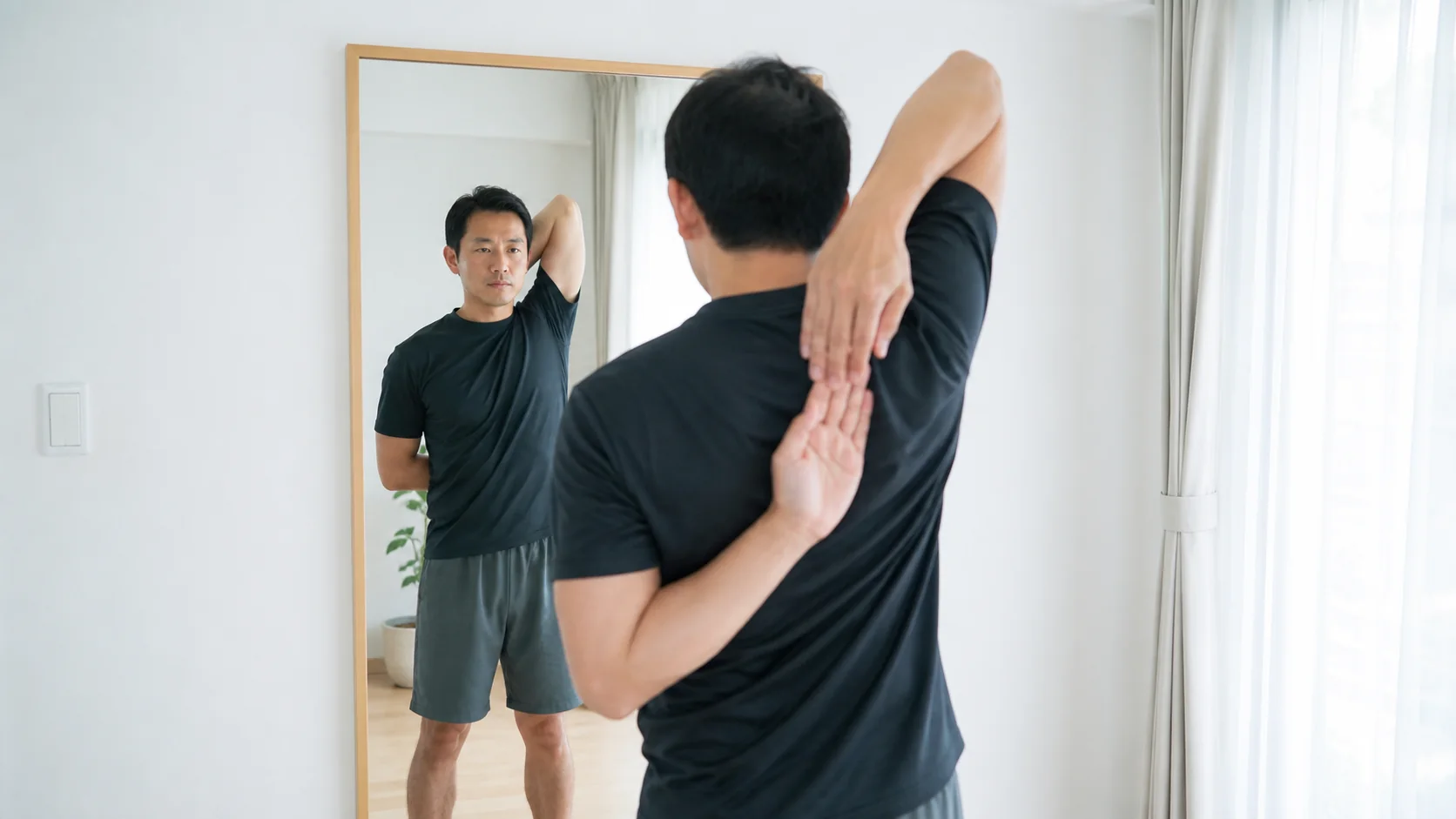 鏡で背中の手の届き方を左右比較する人